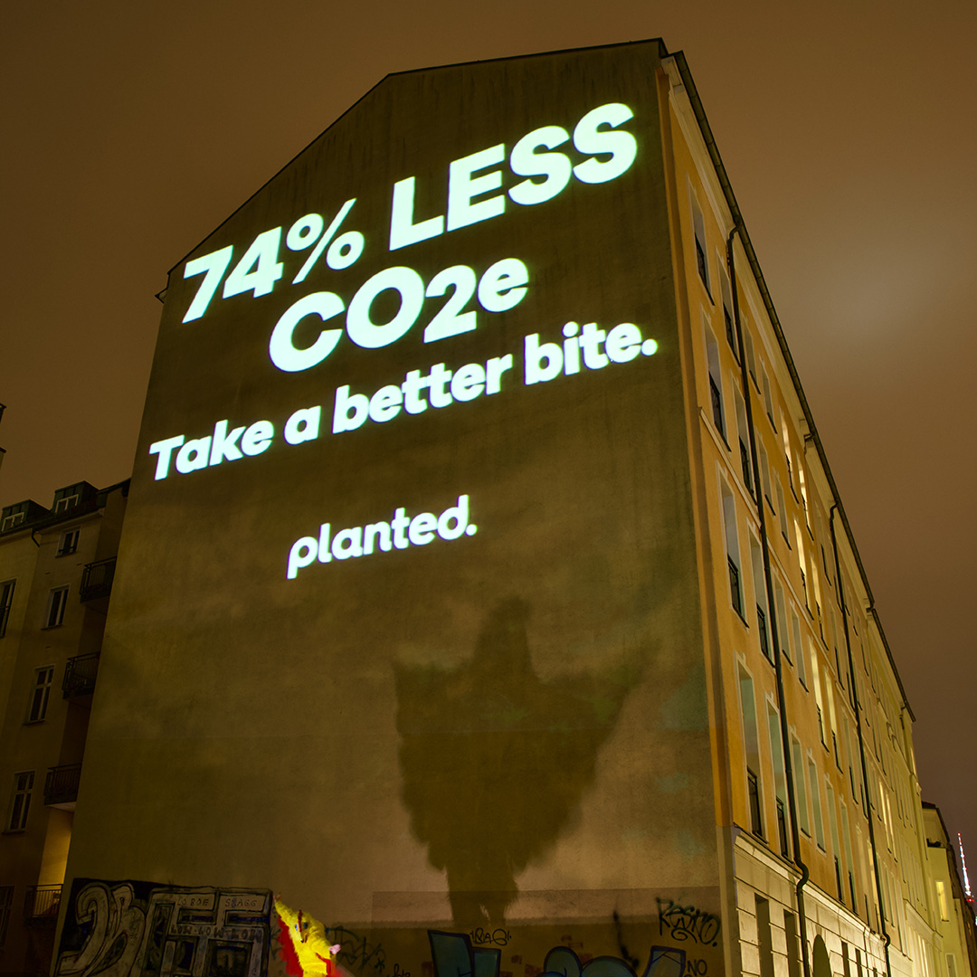 ‘74% less CO₂e. Take a better bite.’ projected onto the side of a tall building